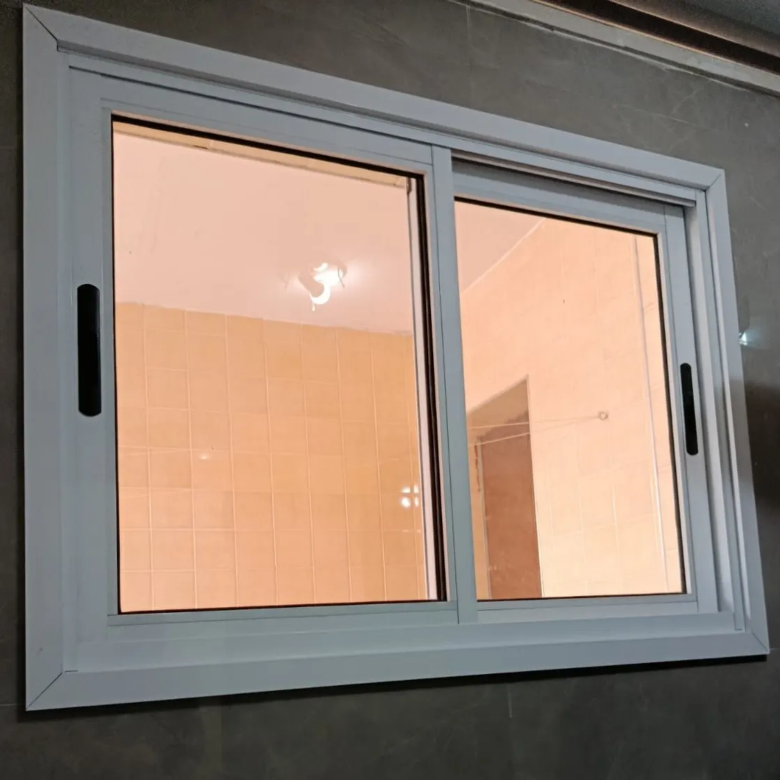 Janela de correr de duas folhas em alumínio branco com puxadores escuros, em banheiro de porcelanato cinza