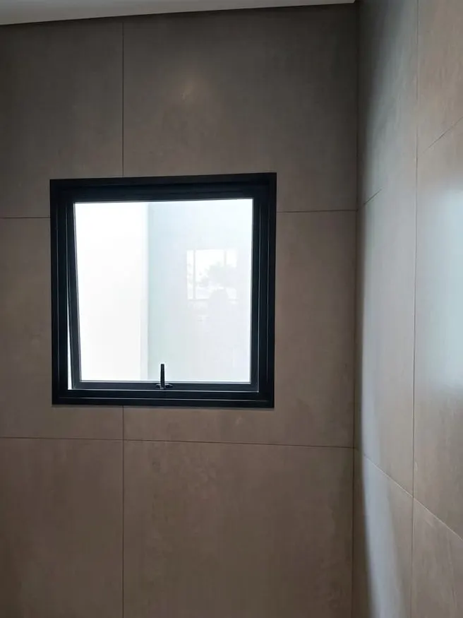 Janela maxim-ar de alumínio preto instalada em parede de porcelanato bege